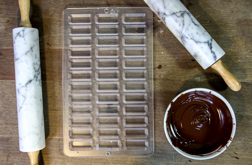 Moule à chocolat ouvert sur un plan de travail en bois avec du chocolat fondu prêt à être coulé