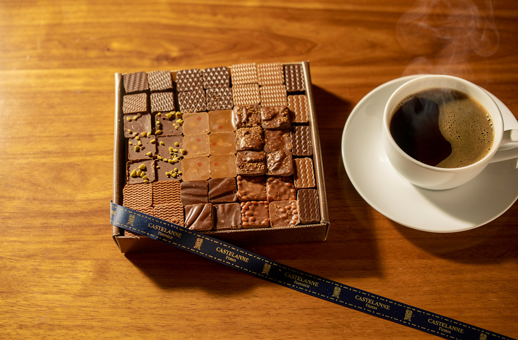 Coffret de chocolats Castelanne ouvert avec assortiment de carrés de chocolats variés sur une table en bois.