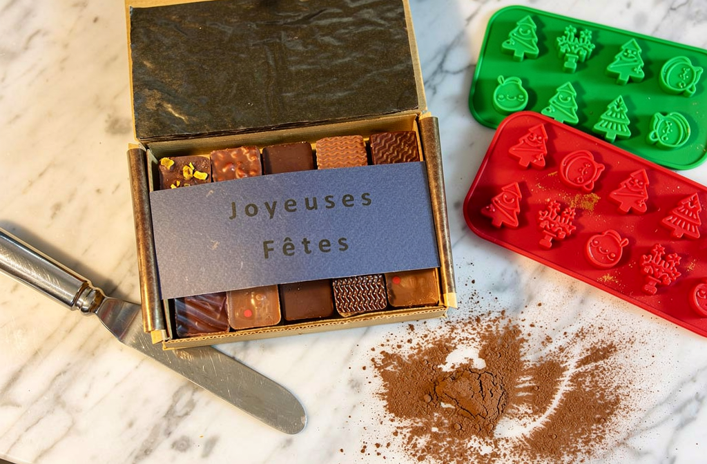 Boîte de chocolats de Noël artisanaux posée sur un plan de travail avec des moules.