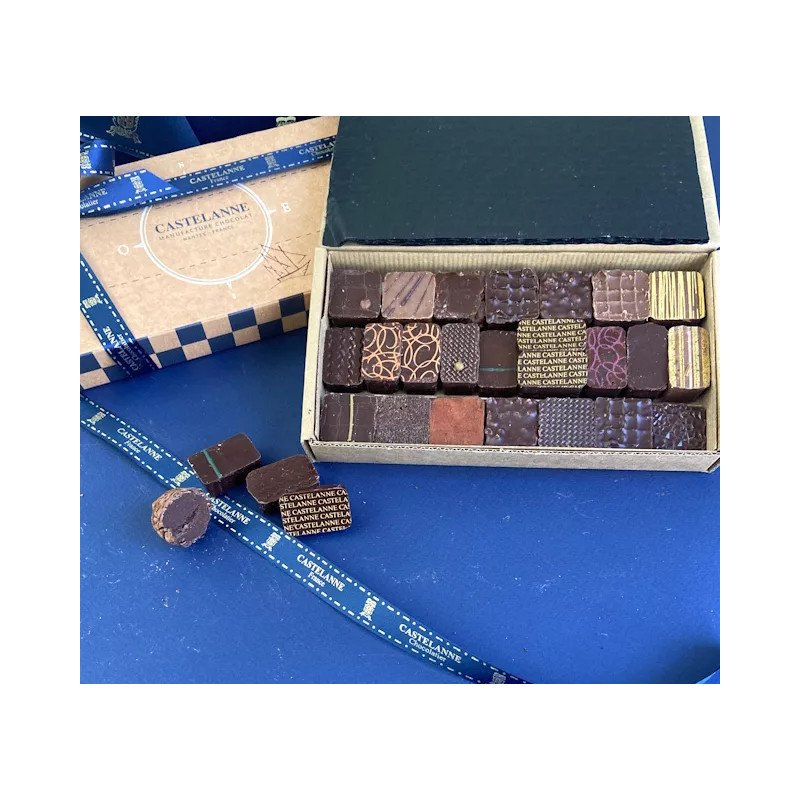 Boîte de chocolats assortis Castelanne artisanaux disposés dans un coffret, sur fond bleu, avec ruban et emballage présentant le nom Castelanne.