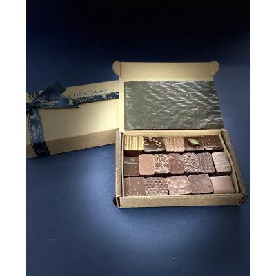 Boîte de chocolats assortis Castelanne façon coffret cadeau, ouverte, montrant des pralines et ganaches artisanales posées dans une caissette beige sur fond bleu.