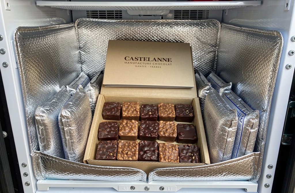 Boîtes et barres de chocolats Castelanne artisanal dans une boîte réfrigérée, emballage argenté et coffret beige portant le logo Castelanne. Boîtes et barres de chocolats Castelanne artisanal dans une boîte réfrigérée, emballage argenté et coffret beige portant le logo Castelanne.