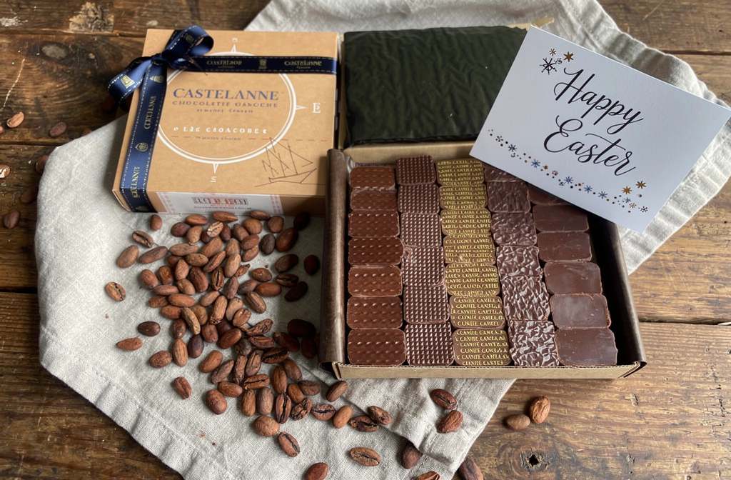 Boîte de chocolats ganaches Castelanne ouverte sur une table en bois, entourée de fèves de cacao pour Pâques.