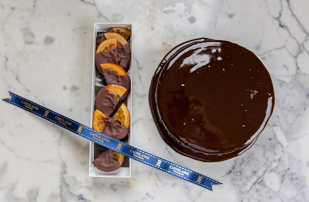 Oranges enrobées de chocolat présentées dans une boîte élégante sur un plan de travail.