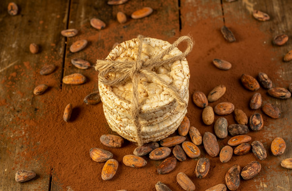 Galettes de riz ficelées posées sur une table en bois avec des fèves de cacao et de la poudre de chocolat.