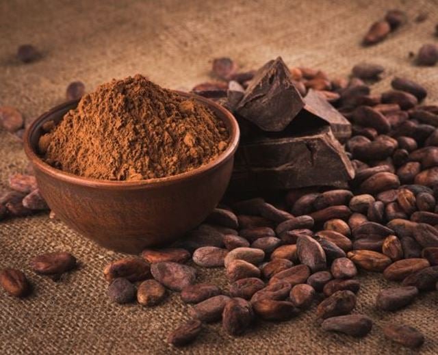 Poudre de cacao et blocs de chocolat sur un sac de jute, entourés de fèves de cacao.