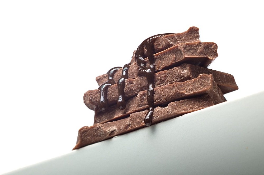Tablette chocolat noir artisanal en morceaux empilés, nappe de ganache sur une assiette blanche